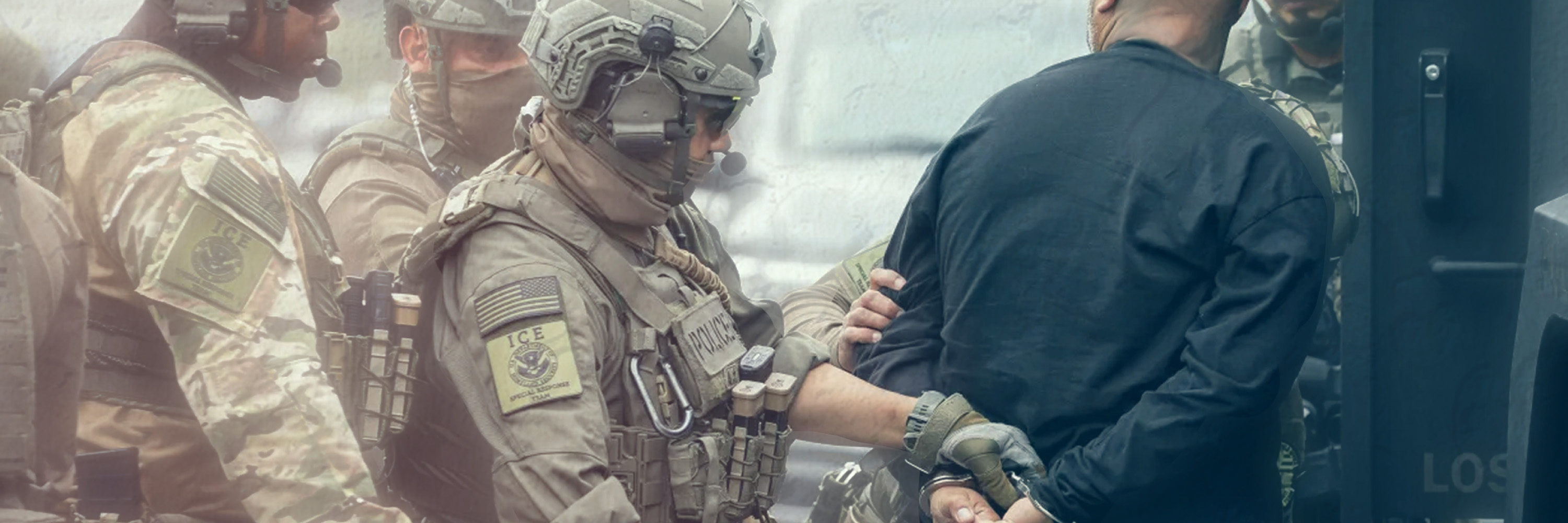 Immigration Customs and Enforcement officers in camouflage surround and handcuff a person.