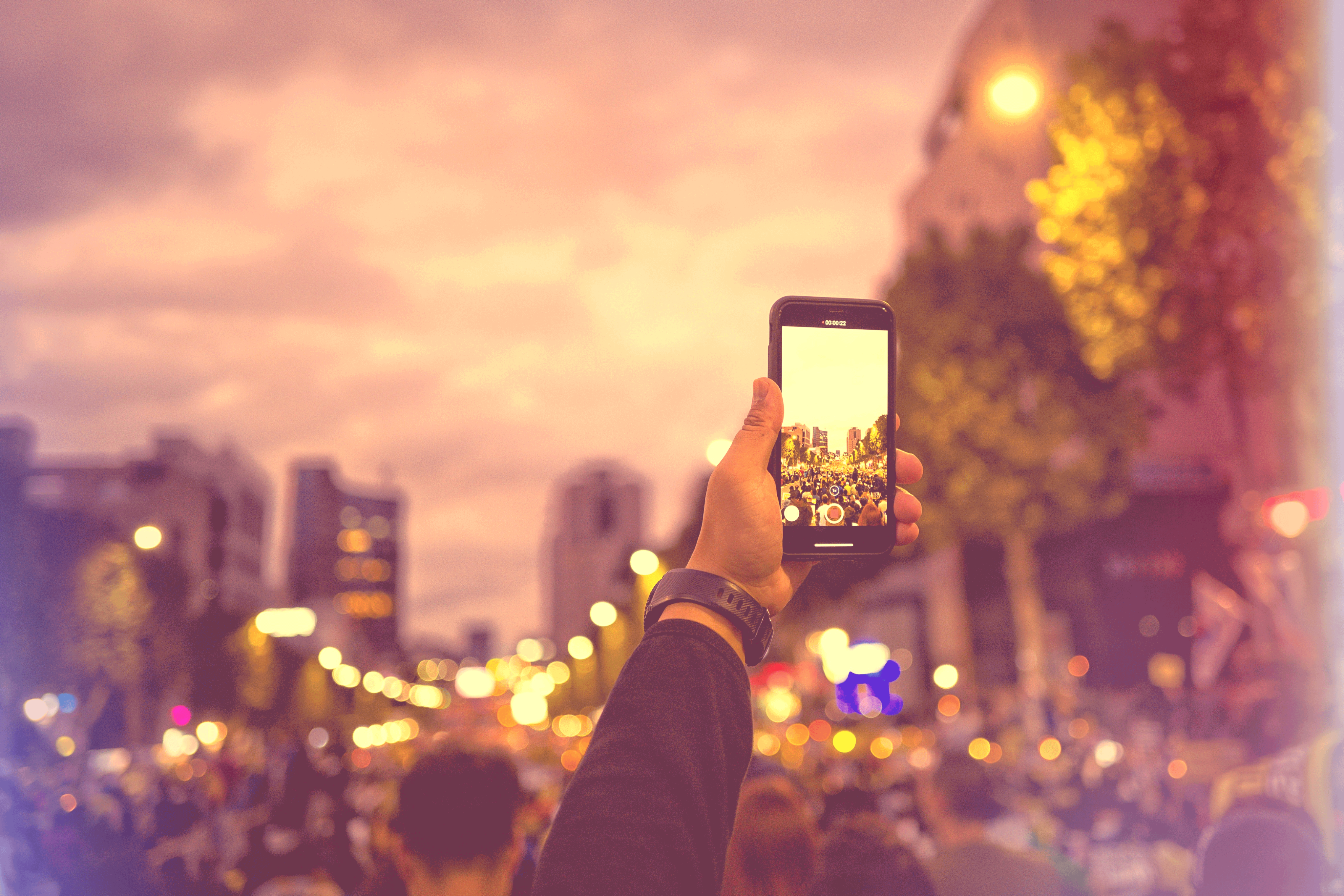 A hand lifts a phone above a crowd to record.